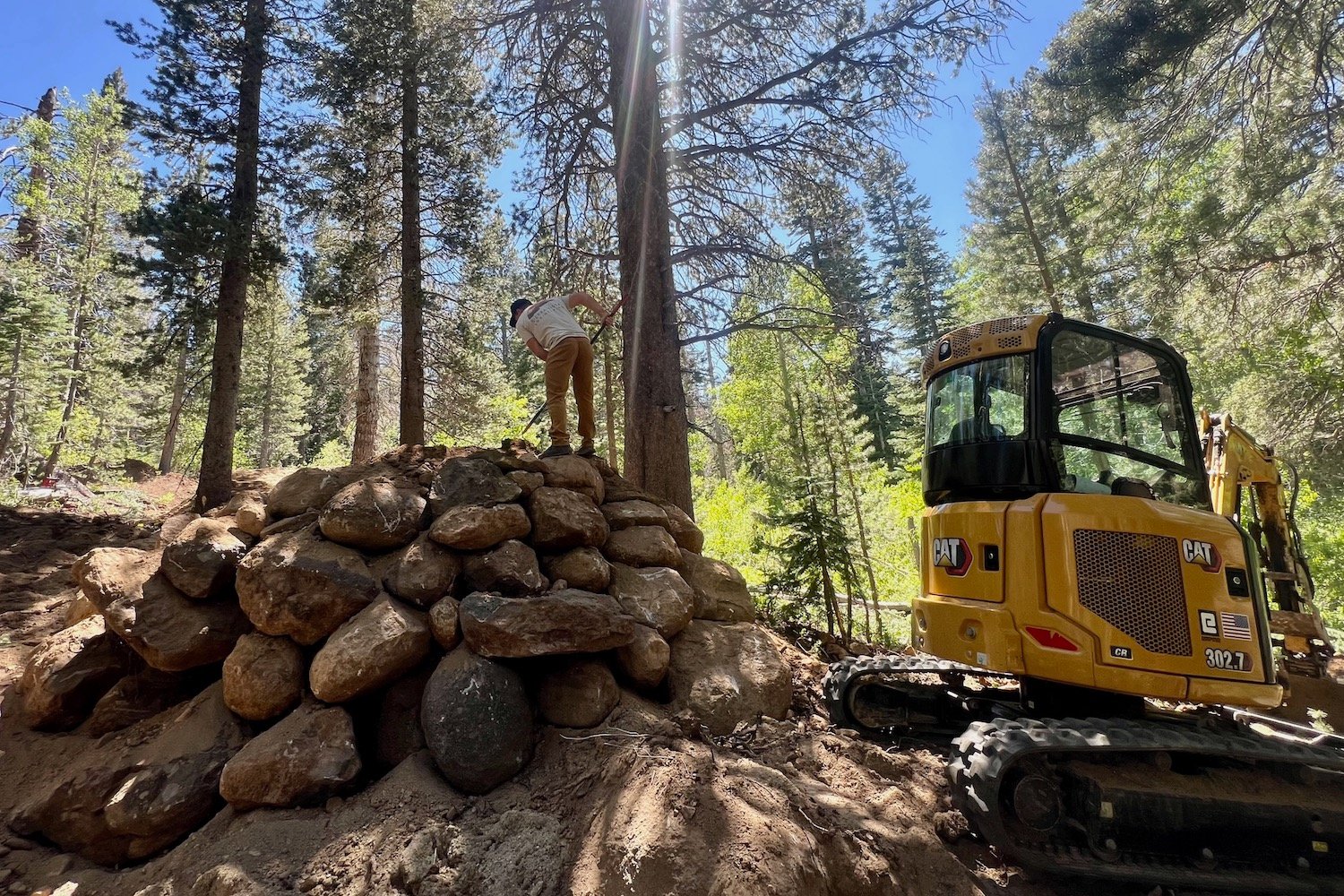steve wentz working on a drop or jump feature with a hand tool with the excavator nearby.