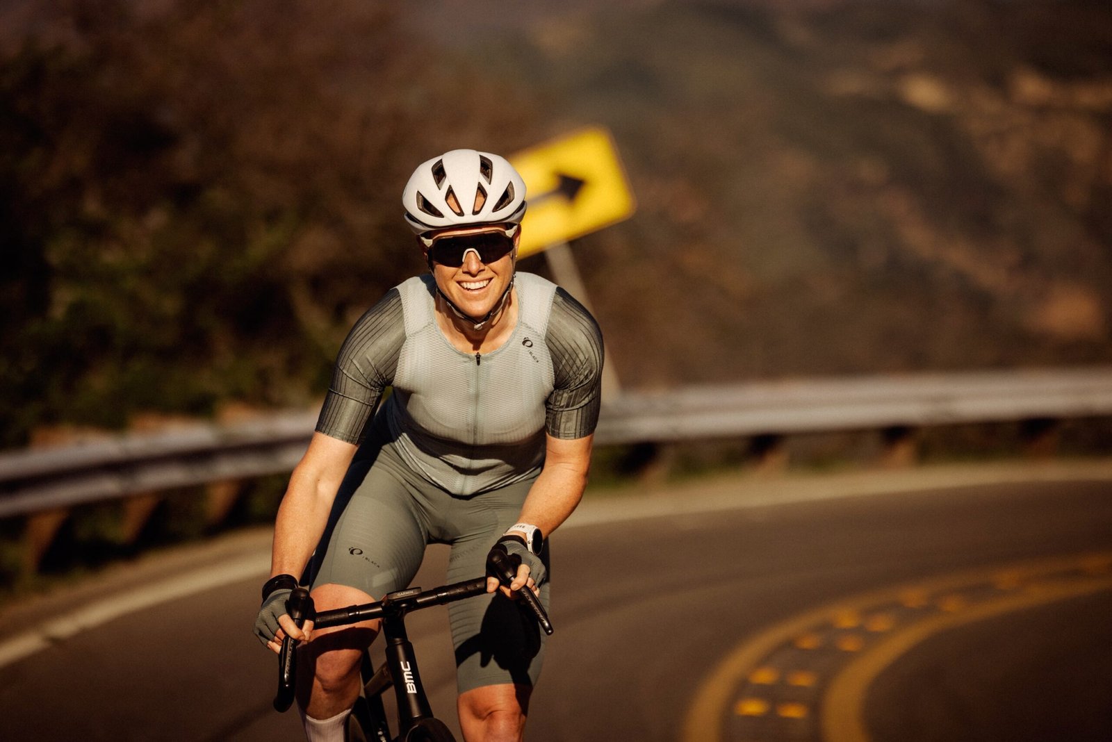 a woman riding up a hill on a road bike wearing the Pi PRO/Black jersey